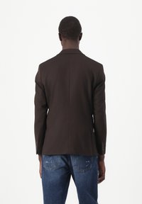 Brauner Blazer mit strukturiertem Design, ausgestattet mit einer einzigen Rückenschlitz und knopfbaren Ärmeln, kombiniert mit blauen Jeans.