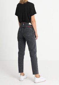 Černé džíny z denimu s vysokým pasem, úzkým střihem a roztrhaným lemem. Mají zadní kapsy a decentní branding na pásu. Spárované s černým tričkem.