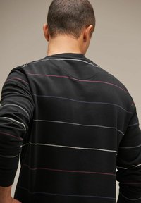 Maglietta nera a maniche lunghe con righe orizzontali in tonalità di bianco, grigio e viola. Tessuto morbido con colletto girocollo e vestibilità rilassata.