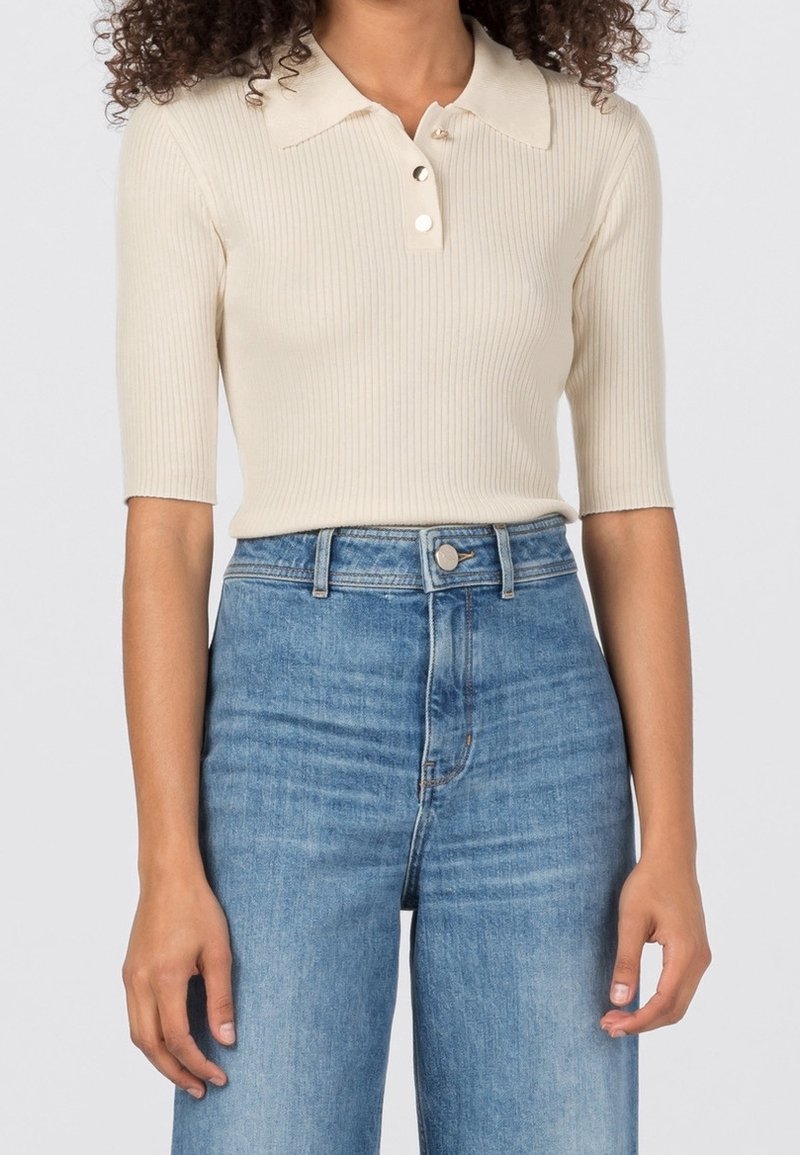 Chemise polo beige à côtes avec un col et une patte de boutonnage à trois boutons, associée à un jean en denim bleu taille haute.