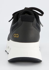 Baskets noires avec une tige en maille texturée, semelle blanche contrastante et un détail de logo doré sur le talon. Fermeture traditionnelle avec lacets.