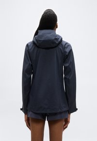 Άτομο που φοράει σκούρο μπλε μπουφάν με κουκούλα και αντίστοιχα σορτς, εμφανιζόμενο από την πίσω πλευρά με φόντο απλό λευκό.