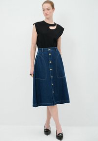 Haut noir à manches courtes avec un détail en découpe, associé à une jupe en denim bleue arrivant au genou avec des poches avant et des boutons dorés.