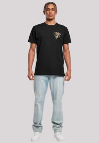 Svart bomulls T-skjorte med et fargerikt grafisk design på brystet, kombinert med lyseblå denimjeans og hvite sko.