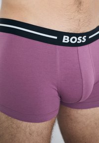 Purple cotton boxer briefs with a black waistband featuring white stripes and "BOSS" logo in bold letters. Smooth texture and fitted design.