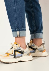 Sportovní tenisky mají síťovaný svršek v krémové, oranžové a šedé barvě s černými akcenty. Silná bílá podrážka s béžovými detaily na outsole.