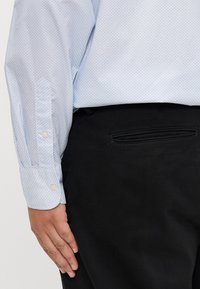 Jasnoniebieska koszula z delikatnym geometrycznym wzorem, z zapięciem na guzik przy mankietach, połączona z czarnymi spodniami z detalem kieszeni z tyłu.