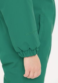 Grøn polstret jakke med elastiske manchetter, en glat tekstur og en sidelomme. Brandlogoet "W-PRO" er broderet i matchende grøn.