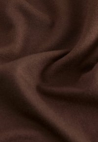 Brauner Baumwollstoff mit einer glatten Textur, der feine Rippungen und sanfte Falten zeigt, wodurch Weichheit und Fall betont werden.