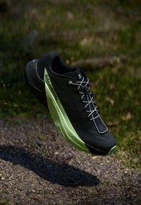 Černá běžecká bota s textura povrchem a zelenými akcenty. Disponuje lehkým designem a jedinečnou, vzorovanou podrážkou pro maximální přilnavost.