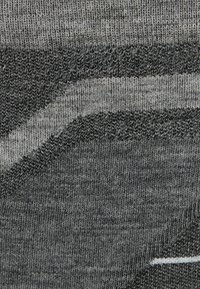 Primer plano de una tela de punto con hilos entrelazados en gris, negro y blanco que forman patrones texturizados diagonales y horizontales.