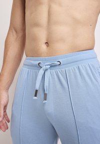 Lichtblauwe joggingsbroek van zachte stof, met een elastische tailleband, trekkoorden en zijzakken. Glad textuur met plooien.