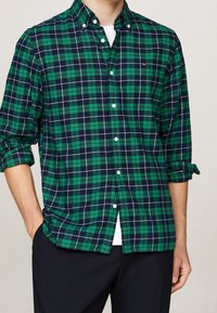 Camicia a quadri verde e blu navy in cotone, con colletto abbottonato e bottoni bianchi, maniche arrotolate e vestibilità rilassata.