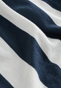 Tamsiai mėlyna ir balta dryžuota medžiaga su tekstūruotu paviršiumi, jungianti pakaitomis plačius ir siaurus dryžius, drapiruota ir šiek tiek susiraukšlėjusi.