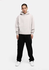 Light gray hooded sweatshirt with a front pocket, paired with black sweatpants. White sneakers complete the casual outfit.