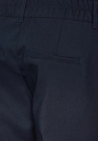 Mörkblå tygbyxor med en slät textur, som har två bakfickor med prydligt sydda kanter och ett elastiskt midjeband.