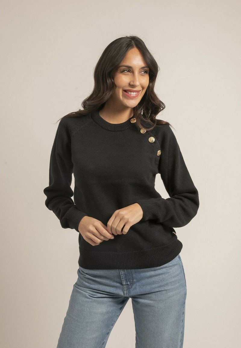 Pull en maille noir avec un col rond, doté de quatre boutons dorés sur l'épaule gauche et de bords côtelés aux manches et à l'ourlet. Assortie à un jean bleu.