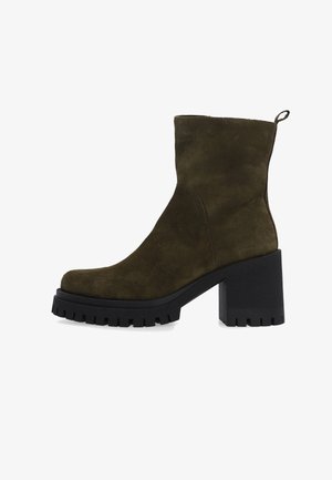 Groene suède enkelboot met een robuuste zwarte plateauhak en een gestructureerde zool, met een eenvoudig ontwerp en stikdetails langs de naad.
