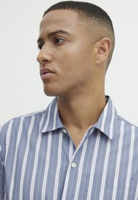 Blauw-wit gestreept shirt, korte mouwen, kraag, knoopsluiting, borstzak aan de linkerkant, katoenen stof met een gladde textuur.
