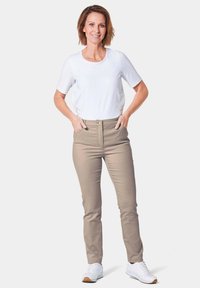 Beige broek gecombineerd met een witte T-shirt met korte mouwen. De broek heeft een slim fit en een knoopsluiting. Sneakers zijn wit met een lichtbruine zool.