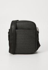 Sac en bandoulière noir avec un tissu texturé, fermeture zip, bandoulière réglable et motif de logo embossé sur le devant.