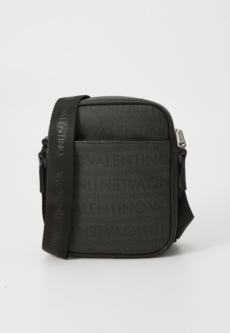 Black crossbody bag featuring a textured fabric, zip closure, adjustable strap, and embossed logo pattern on the front.