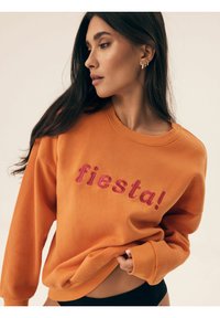 Pomarańczowa bluza z różowym haftem "fiesta!". Posiada okrągły dekolt i długie rękawy, wykonana z miękkiego, strukturalnego materiału.