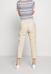 Pantalon beige avec taille élastique, coupe effilée et longueur raccourcie. Associé à un haut rayé à manches courtes et des baskets blanches.