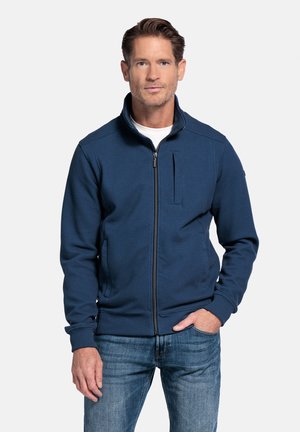 Donkerblauwe zip-up jack van een textuurstof, met een hoge kraag en een borstzak. Gecombineerd met blauwe jeans voor een casual look.