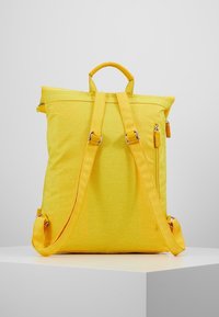 Mochila amarilla con una tela texturizada, correas dobles ajustables, un asa superior y un bolsillo lateral con cremallera. Diseño rectangular simple.