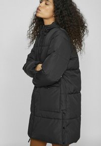 Melnā pūkainā jaka ar kapuci, izšūtu dizainu, priekšējām kabatām un pogām. Iezīme brīva piegrieze un maiga matēta tekstūra.