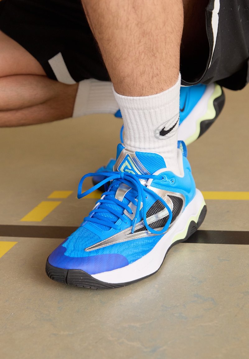 Sportlich Sneakers mit einem hellblauen Mesh-Obermaterial, silbernen Akzenten und einer schwarzen Gummisohle. Verfügt über Schnürsenkel und strukturierte Muster auf der Oberfläche.