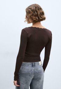 Brun ribstrikket langærmet top med en blonderkant ved halsudskæringen, båret med højttaljede grå jeans med baglommer og en mærkat på linningen.