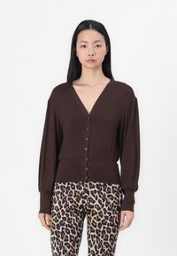 Brun knapp-up cardigan med dyp V-hals, lange ermer og ribbet kant, kombinert med bukser i leopardmønster med en glatt tekstur.