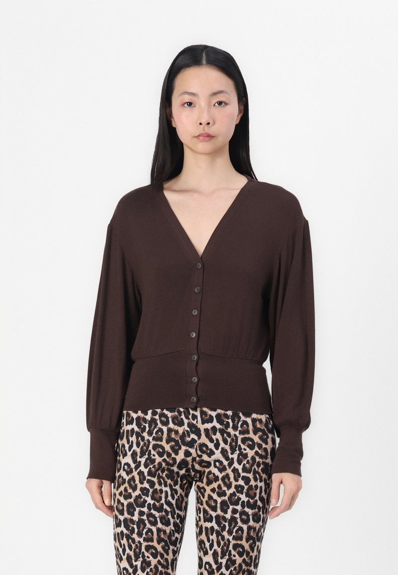 Brun knapp-up cardigan med dyp V-hals, lange ermer og ribbet kant, kombinert med bukser i leopardmønster med en glatt tekstur.
