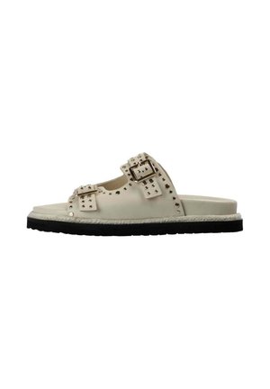 Sandalia beige sin cierre con suela negra, dos correas ajustables con hebilla y pequeñas tachuelas metálicas que decoran la parte superior.