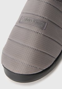 Szürke anyagú Calvin Klein papucs, steppelt mintázattal, texturált fekete talppal és diszkrét logófolttal az oldalon.