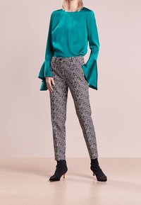 Turkusowa satynowa bluzka z rozkloszowanymi rękawami, w zestawie z dopasowanymi spodniami w czarno-białe wzory. Modelka ma na sobie czarne botki za kostkę.