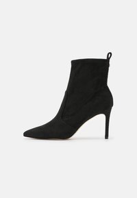 Black suede women’s ankle boot with pointed toe, stiletto heel, and pull tab at the back against a white background.