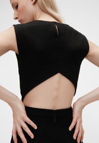 Melns tops ar atvērumu mugurpusē un īsām piedurknēm, ar gludu faktūru un slēptu rāvējslēdzēju vidukļa aizvēršanai.