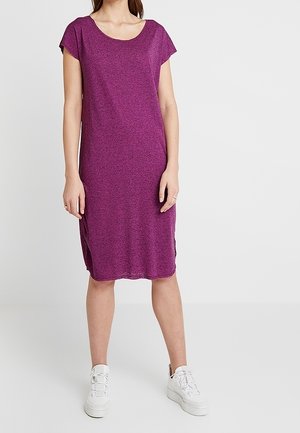 Robe violette, à manches courtes, longueur genou, fabriquée dans un tissu doux et texturé, avec un décolleté rond et des fentes sur les côtés, associée à des baskets blanches.