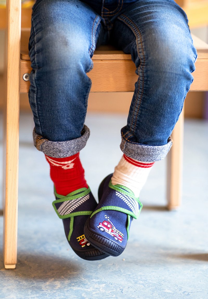 Dunkelblaue Schuhe mit grünen Riemen und Feuerwehrstickerei; getragen mit unpassenden rot-weißen Socken; Kinderjeans mit umgeschlagenen Hosenbeinen.