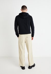 Black hooded sweatshirt with long sleeves, paired with beige wide-leg trousers. The outfit features minimal detailing and classic textures.