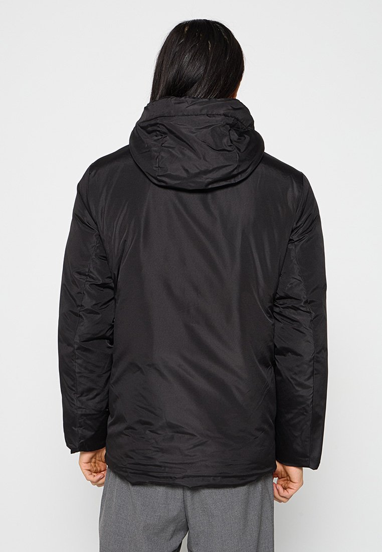 Veste noire matelassée avec capuche, présentant une texture lisse et des coutures piquées. Le dos montre une coupe moderne et un design de longueur mi-longue.