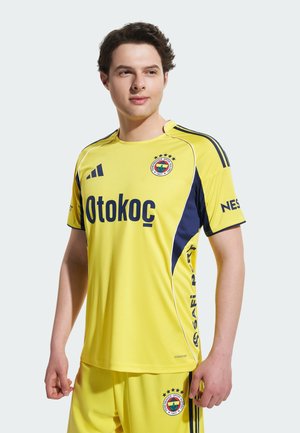 Żółta koszulka sportowa z granatowymi akcentami, z logo "Otokoc", pięcioma gwiazdkami i herbem klubu. Wykonana z lekkiego, oddychającego materiału.
