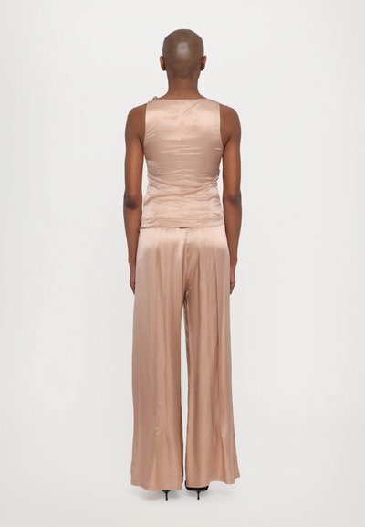 Tuta senza maniche in satin rosa con un busto aderente e pantaloni a gamba larga. Presenta delicate arricciature in vita e una superficie liscia.