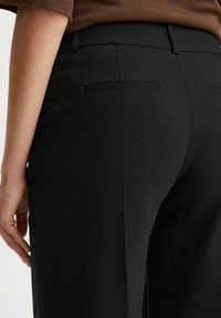 Czarne dopasowane spodnie o gładkiej fakturze, z dopasowanym krojem i dwiema tylnymi kieszeniami. Materiał wydaje się lekki i odporny na zagniecenia.