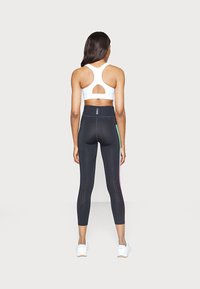 Zwarte sportleggings met kleuraccenten, hoge taille, geperforeerde details bij de kuiten, gecombineerd met een witte sportbeha met een uitgesneden rug.