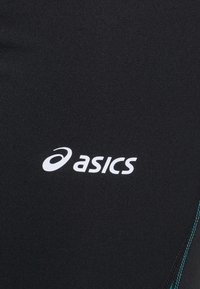 Černé sportovní legíny s texturovaným povrchem, které mají výrazné bílé logo "asics" a tyrkysový akcentní šev.
