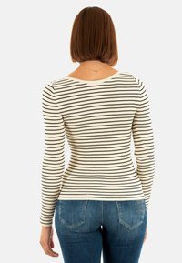 Donna con capelli corti castani che indossa un maglione bianco a coste con righe orizzontali nere e jeans di denim blu, girata di spalle.